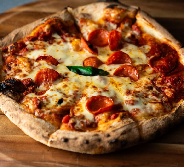 Pepperoni pizza with melted cheese and fresh basil on a wooden surface.