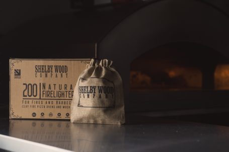 Brown hessian bag with Shelby logo, placed next to a box of firelighters, in a dimly lit room.