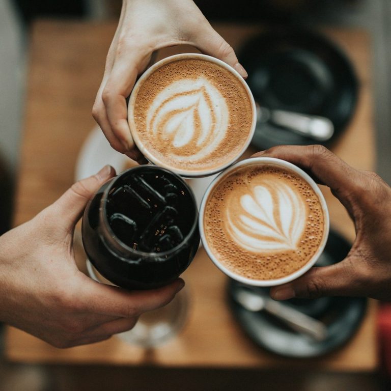 Three cups of coffee clink together, two hot lattes and one iced coffee.