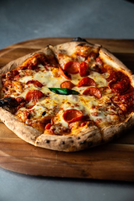 Pepperoni pizza with melted cheese and a basil leaf on a wooden surface.